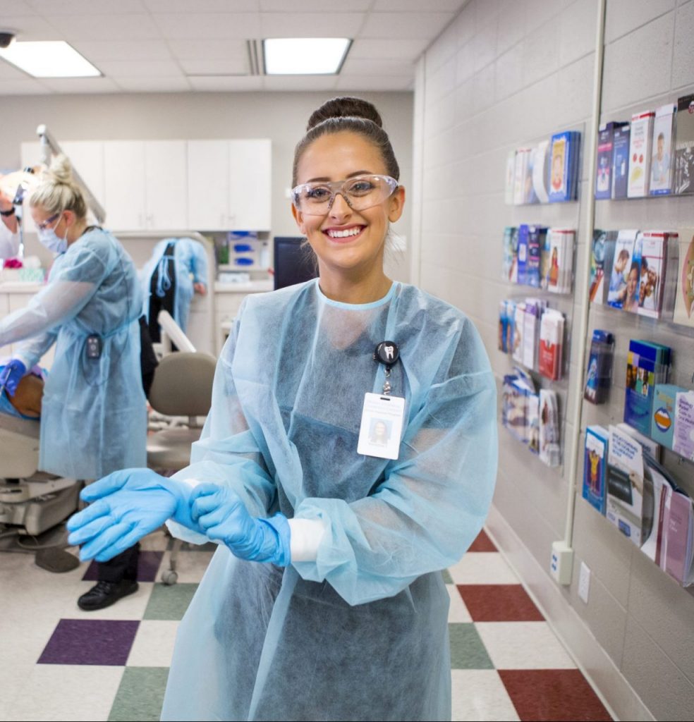 A Dental Assisting student put on gloves while working at a dental clinic