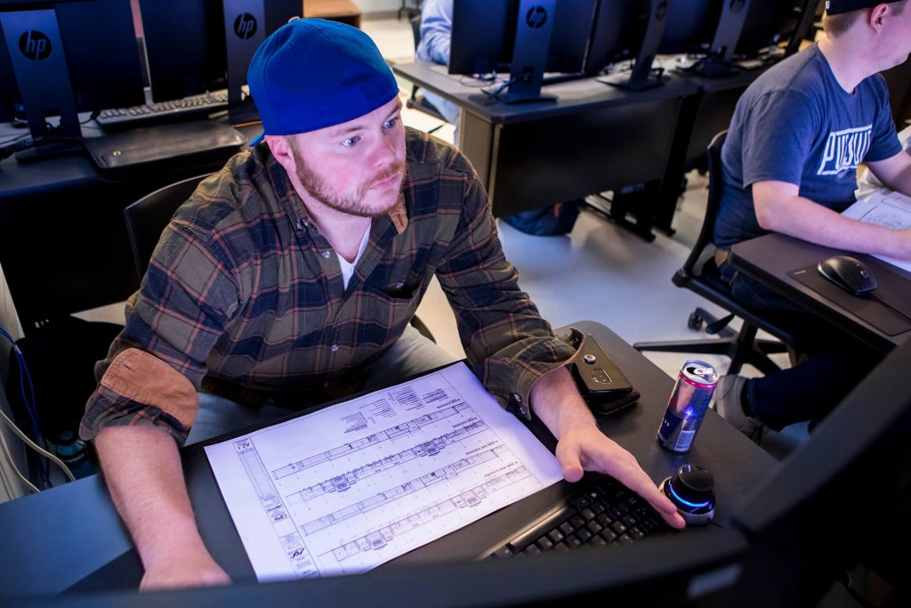 An engineering student using a blueprint for a project in a computer lab