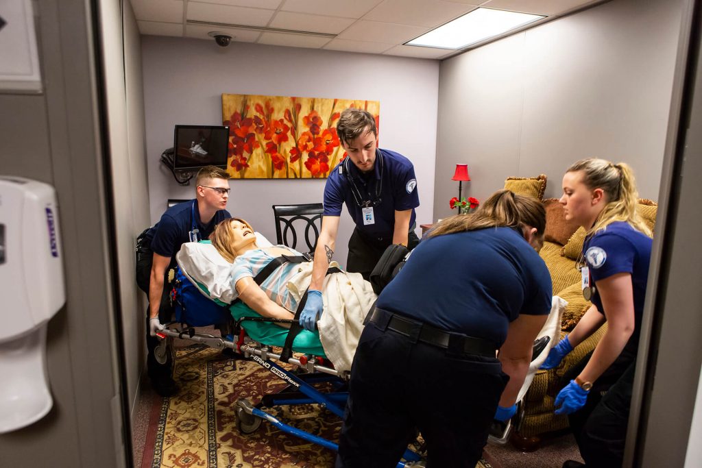 Paramedicine students practicing using a medical stretcher with a practice dummy