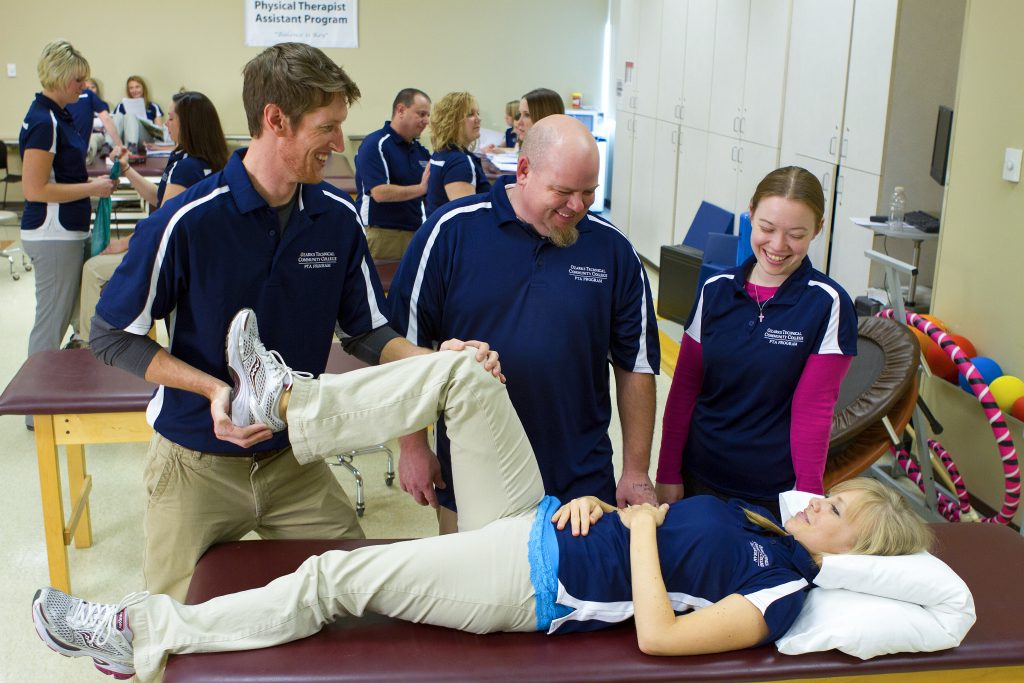 Physical therapy assistant students practicing a leg rehabilitation exercise on another student